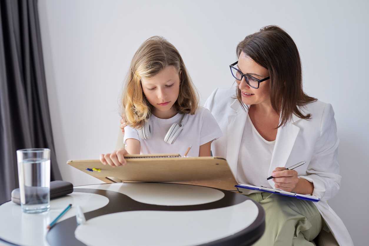 Woman watching young girl draw