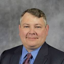 photo of SCC President wearing gray suit, blue shirt and red tie