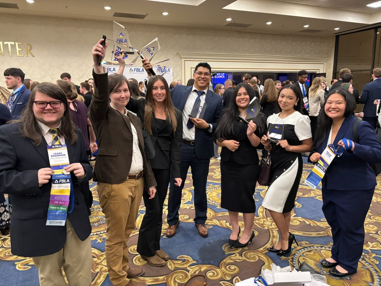 Seven students dressed in professional outfits pose with their FBLA-C awards in Las Vegas.