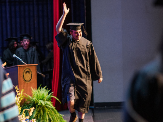 Male Sttudent Walking Across Stage at Graduation to Accept Diploma